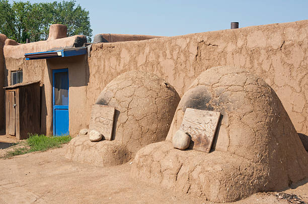 Two Adobe Horno Ovens An outdoor adobe oven or "horno" is used by the Pueblo people for baking bread, pastries and wild game.  A fire is built inside and when it is reduced to ash, the ash is taken out and the raw food is put inside to bake.  Pictured here are two hornos backed by an adobe wall. stove oven adobe outdoors stock pictures, royalty-free photos & images