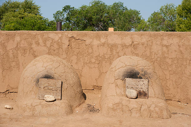 Two Adobe Horno Ovens An outdoor adobe oven or "horno" is used by the Pueblo people for baking bread, pastries and wild game.  A fire is built inside and when it is reduced to ash, the ash is taken out and the raw food is put inside to bake.  Pictured here are two hornos backed by an adobe wall. stove oven adobe outdoors stock pictures, royalty-free photos & images
