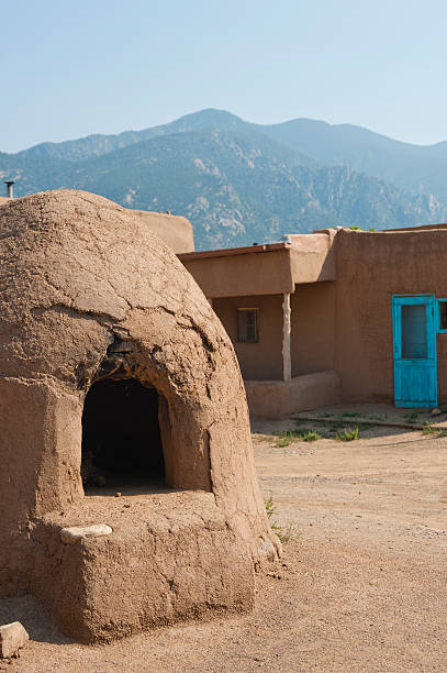 Adobe Horno, Pueblo and Mountains An outdoor adobe oven or "horno" is used by the Pueblo people for baking bread, pastries and wild game.  A fire is built inside and when it is reduced to ash, the ash is taken out and the raw food is put inside to bake. stove oven adobe outdoors stock pictures, royalty-free photos & images