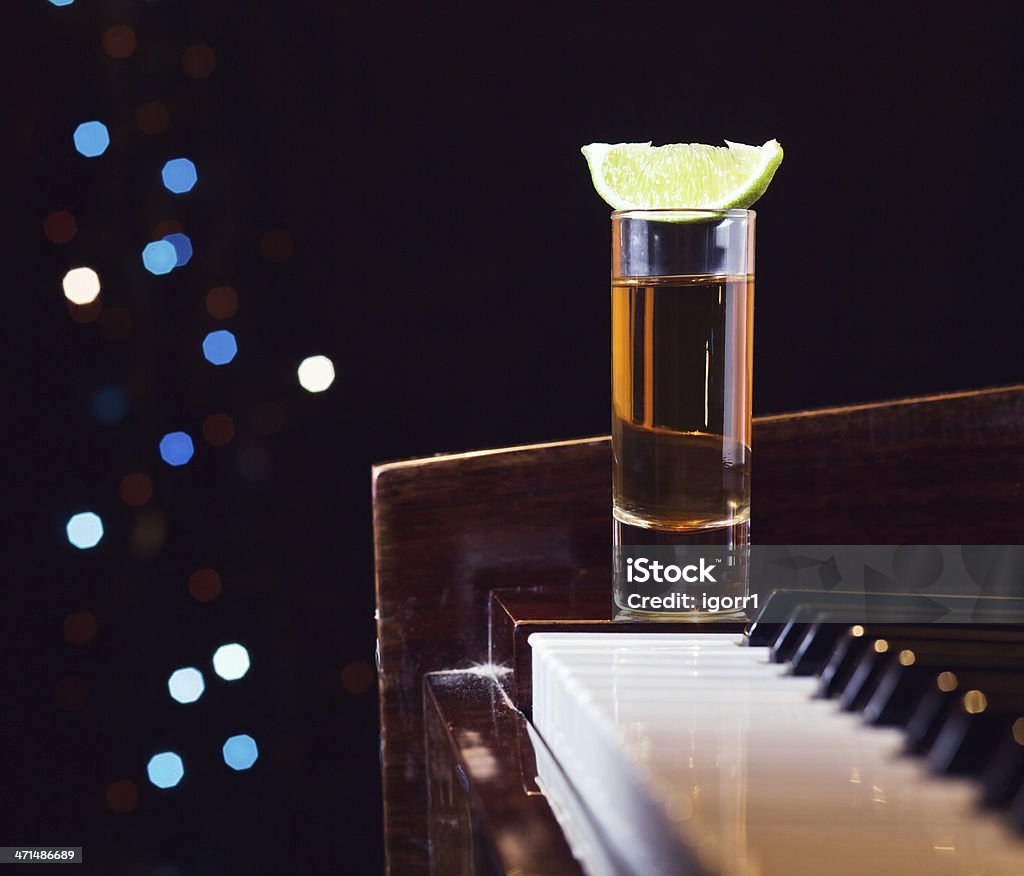 A glass of tequila with a lime on top resting on a piano Gratitude for the maestro, glass with tequila on a piano. Alcohol - Drink Stock Photo