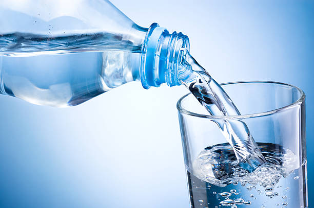 istock Close-up pouring water from bottle into glass on blue background 471488514