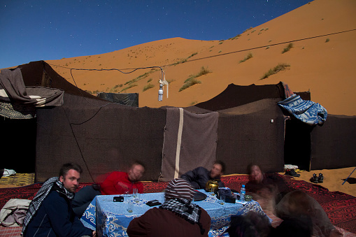 Erg Chebbi, Morocco - March 16, 2011: Sahara sand dunes in Erg Chebbi in Morocco light with moonlight - people are blurred because of the long exposure. On the pictures you can see a group of tourist drinking tea in one of the camps equipped for tourists on desert treks. There are stars on the sky.