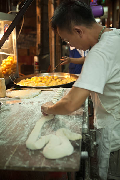 Bankgkok, Thailand - November 16, 2012: A street vendor prepares chinese doughnuts for passersby at his food stall in the Chinatown district of Bangkok, Thailand.