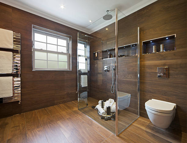 luxury bathroom with wood effect tiles a guest's bathroom in a luxury new home with walls and floor tiled in wood-effect ceramic tiles. A glass screen enclosed shower area sits near the centre with a "rainfall" shower overhead and hand shower attached to the wall. The floor of the shower area is dressed with towels, bathrobe and toiletries for guests. Three white towels are draped over the chrome towel radiator to the left. On the back wall (right) are two recesses, lit by LED lighting, for toiletries and ecorative items such as the candles. faux wood stock pictures, royalty-free photos & images