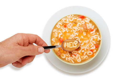 This is an overhead photo of a man scooping out of a bowl of Alphabet Soup with the message on the spoon spelling 