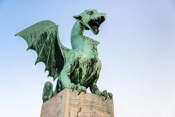 Dragon statue on stone pillar of famous Dragon Bridge, Zmajski Most, in Ljubljana against blue sky. Ljubljana, Slovenia.