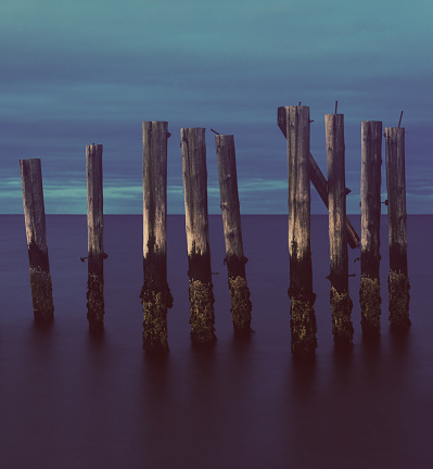 A set of old pier pilings under late evening, overcast skies. Long exposure, slight cross processed toning.