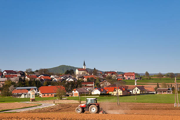 Veliki Gaber, Slovenia - April 25, 2013: Farm tractor working in a field. In the background is a small village Veliki Gaber in Slovenia.