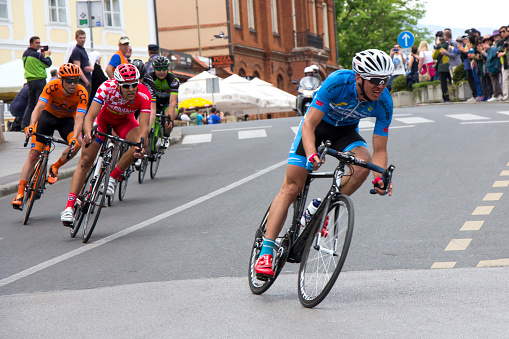 A group of male bicycle racers ride together during a criterium road bike race.  A criterium road bike race is an event where competitors do several laps around a closed circuit usually in a city or urban center.