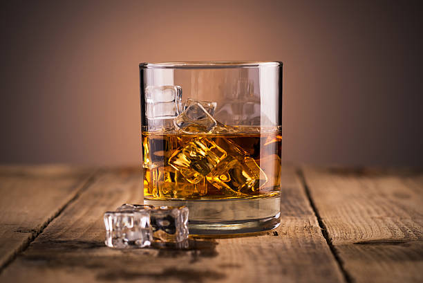Glass of whiskey Whiskey in a glass over ice cubes, on wooden table wet wood texture stock pictures, royalty-free photos & images
