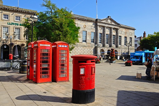 Stafford, United Kingdom - September 11, 2014: Red post box and telephone boxes with the Shire Hall Gallery to the rear in Market Square and people passing by, Stafford, Staffordshire, England, UK, Western Europe.