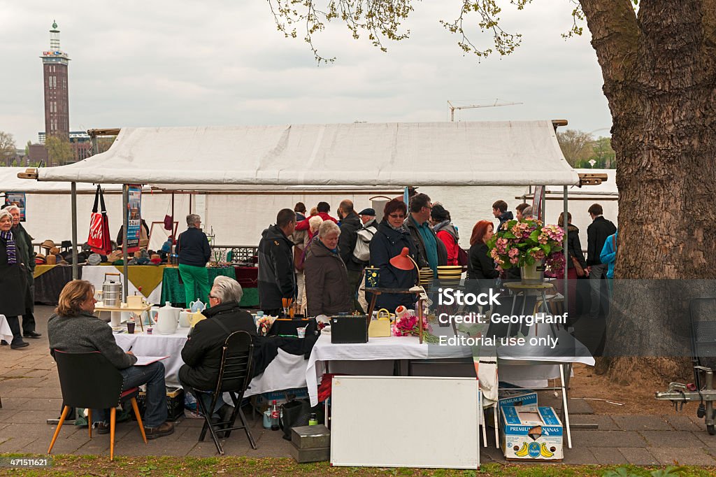 Flea Market in Cologne Cologne, Germany - April 28, 2013: People visit a flea market on the "Rheinuferstrasse" in front of the Hohenzollern Bridge in Cologne. In the background the Rhein can be seen. Many look at the antiques or just go for a walk. In the background the old Rheinhallen are seen with exhibition tower on the Rhine in Cologne Deutz. In the halls of the German television channel RTL is at home. Ancient Stock Photo