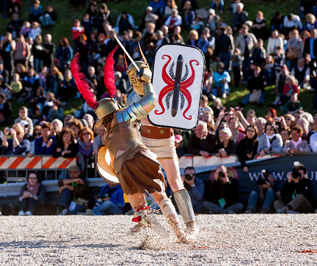 Rome, Italy - April 21, 2013: Gladiators fighting in historical costumes with ancient weapons in Circo Massimo, Rome, during Rome's Foundation Celebrations. The woman is attacking with her sword while the other gladiator lifts his shield. Even though not very commonly, women from Gallia or Keltia were sometimes employed as gladiators because of their speed and agility. Gladiators' fighting was one of the most required entertaining activity. This event has been organized by Gruppo Storico Romano and involved 11 different countries, 2000 people and 53 different volunteer associations. All the costumes are historically correct thanks to the supervision of a team of archeologists and researchers. The leading volunteer group of Gruppo Storico Romano was born in 1994. By now, the group has highly increased and has a scientific department of experimental archeology which expresses itself by recreating ancient situations such as parties or gladiators' fights and dances.