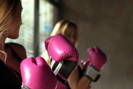 Young blonde boxing woman training in front of a mirror, soft focus low exposure in studio shot