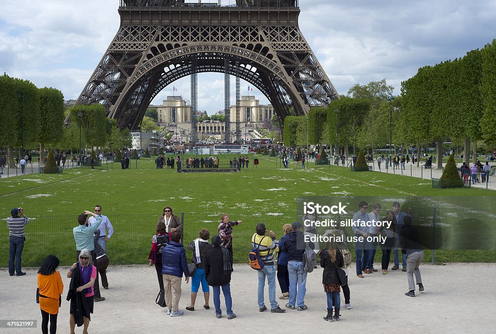 People in Champ de Mars park with the Eiffel Tower Paris, France - May 12, 2013: People in the Champ de Mars park in front of the Eiffel Tower. Some are striking a pose to have their picture taken with the Eiffel Tower in the background. The grass of the lawn - and the foliage of the trees - in the park are spring green. The Palais de Chaillot at the Trocadéro is seen in the background across the River Seine. Crowd of People Stock Photo