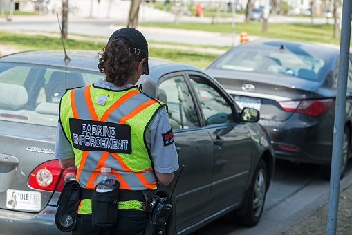 Halifax, Canada - May 8, 2013: A parking enforcement official with Securitas writes parking tickets for vehicles at expired street meters.