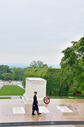 Arlington, United States - May 11, 2013: A single soldier of the ArmyÕs 3rd Infantry Regiment serves as Sentinel at the Tomb in the rain at the Tomb of the Unknowns at Arlington National Cemetery near Washington DC. He is walking the mat past the tomb where a memorial wreath has been placed.