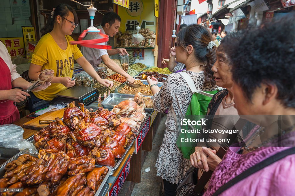 China women buying food at street stall market Shanghai Shanghai, China - 9th October 2012: Women buying local delicacies from a busy street market stall in the crowded alleyways of Qibao, a historic water village outside Shanghai and popular visitor attraction for Chinese tourists. Food Stock Photo