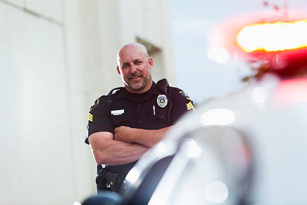 istock Happy police officer standing next to cruiser 471524334