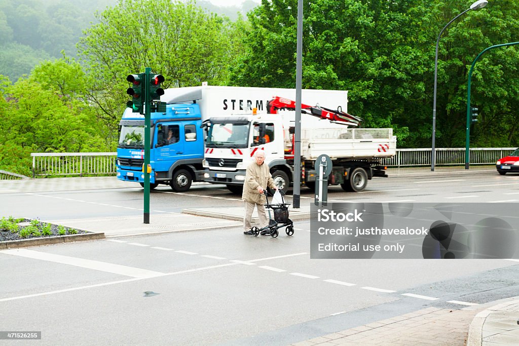 Walk at red light Essen, Germany - May, 17th 2013: Senior man with walking frame is crossing street and traffic light with pedestrian crossing at red light. In background is ruling traffic, there are two trucks. Scene in district Werden of Essen. Adult Stock Photo