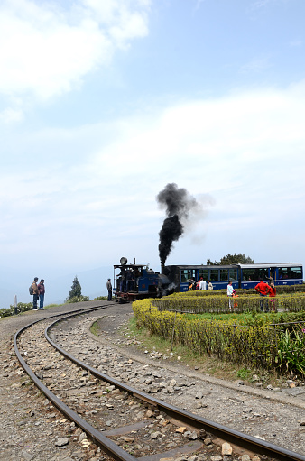 Batasia, Darjeeling, India - April 4, 2011: Steam engine Toy Train has just stopped at the Batasia War Memorial in Darjeeling District(West Bengal); people sitting in the trainn and walking in the park