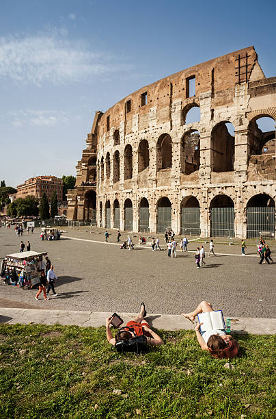 Rome, Italy - May 18, 2013: People relaxing and reading books and kindle under the Coliseum, in Rome.