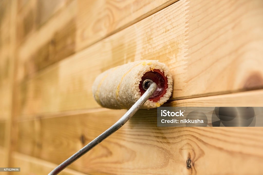Painting the wooden wall with a paint roller Painter covers wooden house with a protective varnish 2015 Stock Photo