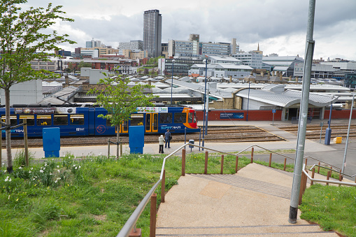 Sheffield, Yorkshire, UK - May 10th 2013: People waiting for tram outside Sheffield railway station. City center skyline and Hallam university buildings are in background. In the foreground are the steel steps built completed in June 2011 which link the city to the Park Hill estate. 