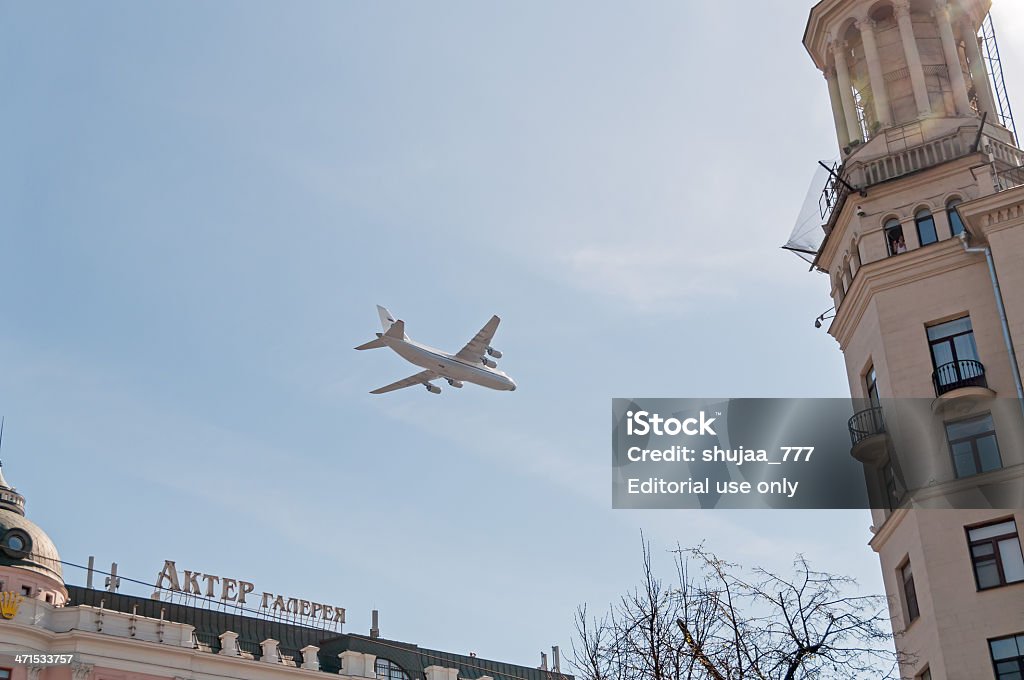 An - 124 Ruslan aereo vola sopra gli edifici contro cielo di sfondo - Foto stock royalty-free di Aereo di linea