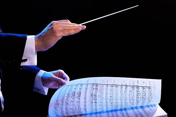 Music conductor using stick and turning the sheet music page Conductor's hands with a baton and music score conductors baton photos stock pictures, royalty-free photos & images