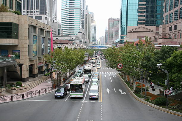 Shanghai, China - October 21, 2005: Crossroads in modern part of Shanghai with Impressive Skyscrapers, China. Cars and Busses wait at the traffic light. Green Trees grow at the streetside.