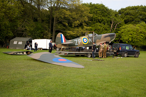 Henley on Thames, England - May 19, 2013: Spitfire being laoded onto a trailer. World War ii Spitfire being loaded onto a trailer. The wings are detached and are on the ground. People in old RAF uniforms help load the plane onto the trailer. A Land Rover car is hitched and ready to tow the aircraft away once secure. A green tent and white trailer are in the background in front of the trees.