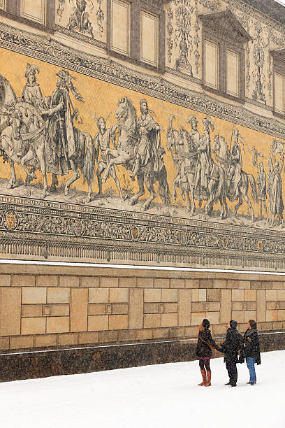 Dresden, Germany - February 23, 2013; tourists watching the Procession of Princes, in German Die Furstenzug, a large mural of a mounted procession of the rulers of Saxony. The mural, with a length of 102 metres, is known as the largest porcelain artwork in the world and is located on the outer wall of the Stables Courtyard of Dresden Castle.