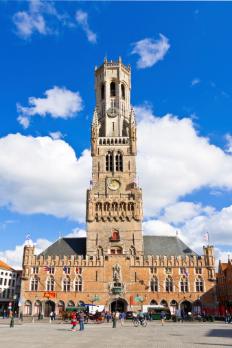 Bruges, Belgium - June 22, 2012: The Belfry (Belltower) in Market Square (Markt) in historic city center. It is a medieval bell tower that  formerly housed a treasury and the municipal archives, and served as an observation post for spotting fires and other danger. In the 16th century the tower received a carillon, allowing the bells to be played by means of a hand keyboard. Bruges has most of its medieval architecture intact and has been a UNESCO World Heritage Site since 2000. Tourists are walking around.