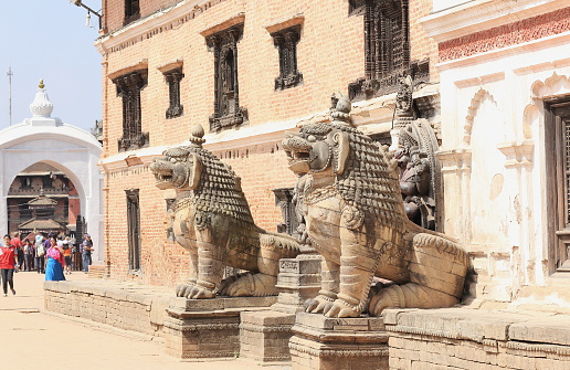 Bhaktapur, Nepal - October 5, 2012: Stone lions -Narsingha- and monkeys -Hanuman- guard the entrance to the National Art Museum while locals and tourists mingle at the Lion Gate of the Durbar Square on October 5, 2012 in Bhaktapur-Kathmandu Valley-Nepal.