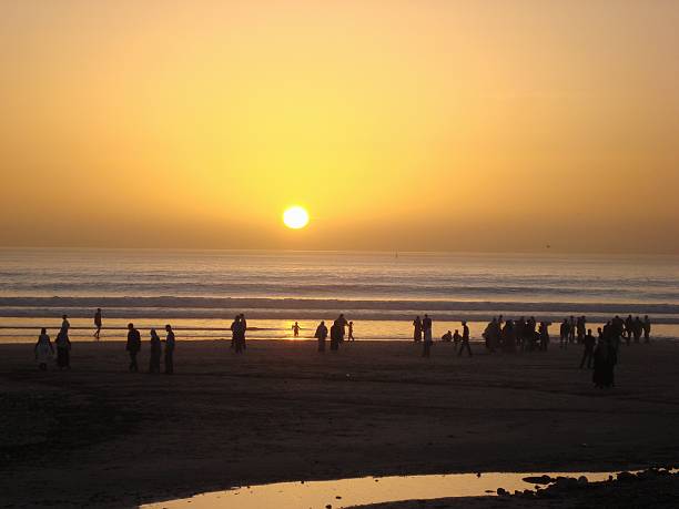 Agadir sunset, Morocco Agadir, Morocco - January 18, 2010: Agadir beach at sunset. local people and tourists walking on the long beach admiring the beautiful sunset sunset agadir marocco stock pictures, royalty-free photos & images