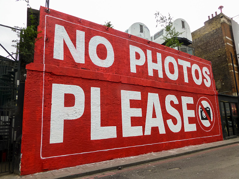 London, UK - 17 May 2013: A 'No Photos Please' graffiti sign on a wall in East London near Shorditch High Street. This wall is often changing with different graffiti on a regular basis and makes for an interesting walk.