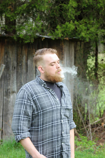 istock Man Blows Smoke in Front of Outhouse 471548634