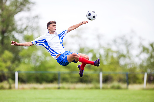 Young soccer player taking a football shot while being in mid air.