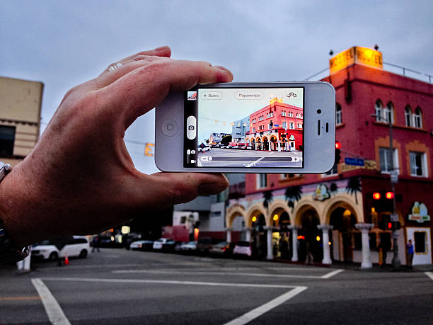 Venice, USA - April 30, 2013: Man holding iPhone 4s and making photo of Venice main Sign illuminated at the evening.