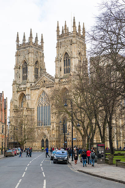 York, UK - March 29, 2013: Street view from Dumcombe Place showing York Minster at the back and pedestrians walking by. The cathedral dates back from 1291.