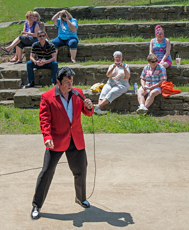Lake George, United States - June 1, 2013: An Elvis look-a-like wearing a red sport coat is performing before an outdoor group of people in Lake George, United States.