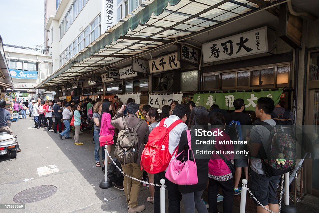 Tsukiji Fish Market Tokyo, Japan - June 3, 2013: People queuing outside the seafood restaurants at Tsukiji Fish Market. Tsukiji Fish Market is the biggest wholesale fish and seafood market in the world. The market is located in central of Tokyo, and is a major attraction for foreign visitors. People In A Row Stock Photo