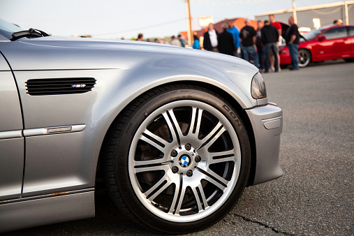 Dartmouth, Nova Scotia, Canada - June 6, 2013: The front wheel of a BMW M3 E46 while parked in a parking lot.  Wheel features the BMW logo as well as a small M logo.  People are visible in background admiring the many cars.  The E46 M3 was first introduced in 2000 and features 333 HP from a 3.2 litre engine.  The BMW M3 is considered one of the best sports cars of all time and is a benchmark in sports performance.