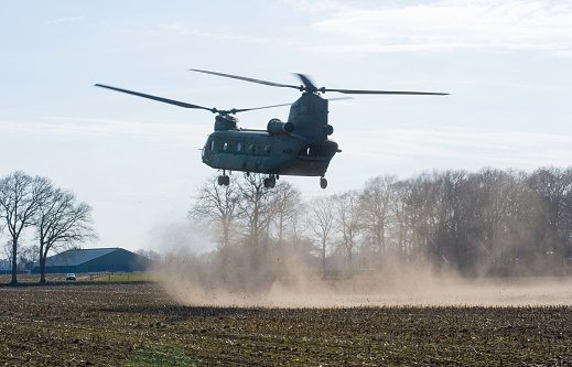 Geesteren, Netherlands - March 25, 2013: A Dutch Chinook helicopter is about to land on a field near a farm to pick up military soldiers during a training, March 25, 2013.