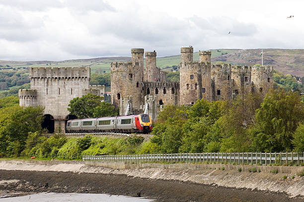 This Virgin Train in the welsh countryside passes a Castle Conwy, Wales - June 2, 2013: Conwy Castle a Virgin Train travelling through the welsh countryside. Conwy Castle and a Virgin Train travelling through the welsh countryside. The railway embankment meets the sea and is covered with trees and shrubs but you can still see the Virgin Voyager diesel high speed train service as it passes the medieval castle at Conwy on the North Wales coast. At Conwy the railway tunnel is made to look like the castle blending the modern with the ancient conwy castle stock pictures, royalty-free photos & images