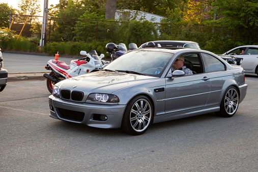 Dartmouth, Nova Scotia, Canada - June 6, 2013: A BMW M3 E46 driving into a parking lot.  Driver visible through window.  In background, some other cars and motorcycles are visible.  The E46 M3 was first introduced in 2000 and features 333 HP from a 3.2 litre engine.  The BMW M3 is considered one of the best sports cars of all time and is a benchmark in sports performance.