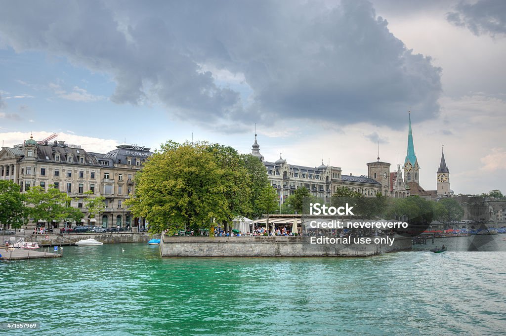 Limmat river and Zurich, Switzerland Zurich, Switzerland - July 25, 2012: View of the old town part of the city of Zurich along the River Limmat. The left side of the river can be seen the two clock towers of the gothic style church with. Tourist and recreational boats line of the river side. People can be see walking or seating along the sidewalks that border the river. Architecture Stock Photo