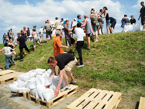 Torgau, Germany - June 7, 2013: Group of people is fighting flood water by raising a protection rampart. Helpers of any age an constitution working hand in hand forming a human chain to stack sandbags on the dam. State of emergency in many regions along the Elbe river in Saxony, Germany.