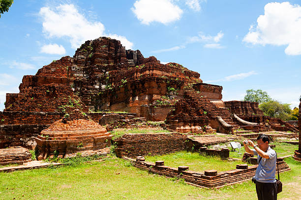 Ayutthaya, Thailand - June, 8th 2013: Asian tourist is standing in courtyard of Wat Mahathat in Ayutthaya and is taking photos. In background is ruin of old huge pagoda.